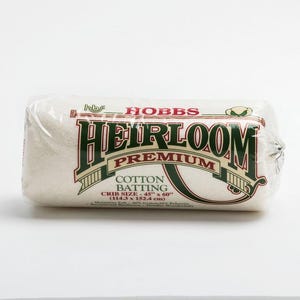 May include: A roll of white Hobbs Heirloom Premium cotton batting in clear plastic packaging. The label reads Crib Size - 114.3 cm x 152.4 cm. The batting is a blend of 80 percent cotton and 20 percent polyester, designed for quilting projects.