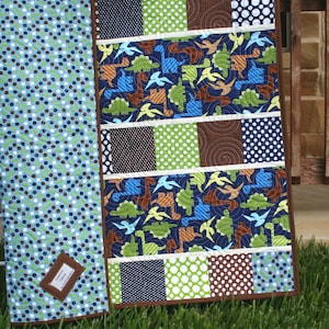 Easy PDF baby quilt pattern with whimsical dinosaur fabrics, polka dot charm squares, and clean strip piecing for beginner quilting projects.
