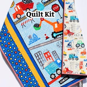 May include: A blue, yellow, and red quilt kit featuring construction vehicles and buildings. The quilt has a blue border with colorful circles and the words "Quilt Kit" are visible. The quilt measures approximately 40 x 50 inches.