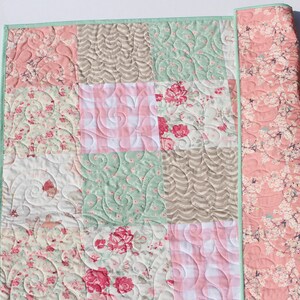 Puede incluir: Una colcha de retazos con un dise&ntilde;o floral en tonos rosa, verde y marr&oacute;n. La colcha est&aacute; hecha de diferentes telas y tiene un patr&oacute;n acolchado.
