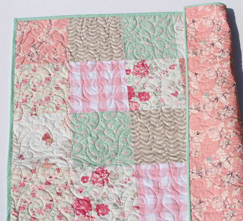 Puede incluir: Una colcha de retazos con un dise&ntilde;o floral en tonos rosa, verde y marr&oacute;n. La colcha est&aacute; hecha de diferentes telas y tiene un patr&oacute;n acolchado.