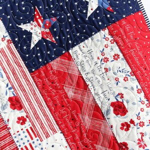May include: A red, white, and blue patriotic quilt with a star pattern and the text "Home of the Free United States of America Home of the Brave Stars & Stripes Let Freedom Ring Land of the Brave" repeated throughout.