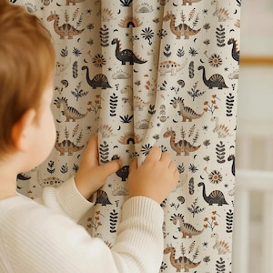 Könnte beinhalten: Beige Vorhänge mit Dinosaurier-Motiv, mit einem sich wiederholenden Muster aus verschiedenen Dinosauriern, Pflanzen und Himmelselementen in Braun, Schwarz und Creme. Die Vorhänge sind aus weichem Stoff und für ein Kinderzimmer geeignet.