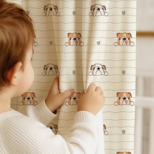 Könnte beinhalten: Cremefarbener Vorhang mit einem sich wiederholenden Muster aus Cartoon-Bulldoggen-Gesichtern in Braun, Weiß und Orange, durchsetzt mit kleinen Herzen. Der Vorhang hat horizontale Streifen. Die Hände eines Kindes halten den Vorhang.