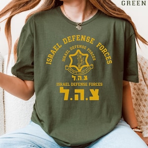 May include: Military green t-shirt with the text "ISRAEL DEFENSE FORCES" in gold. The shirt displays a circular emblem with Hebrew and English text. The bottom of the shirt also has the Hebrew letters "צ.ה.ל" in gold.
