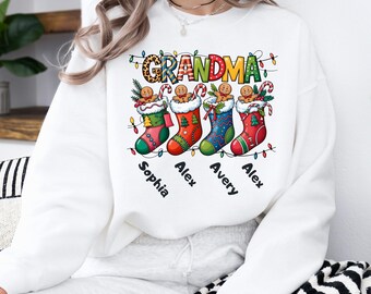 May include: White sweatshirt with a Christmas-themed design. The design features the word "GRANDMA" above four Christmas stockings, each with a gingerbread man and a name: Sophia, Alex, Avery, and Alex. The word "WHITE" is in a black oval.