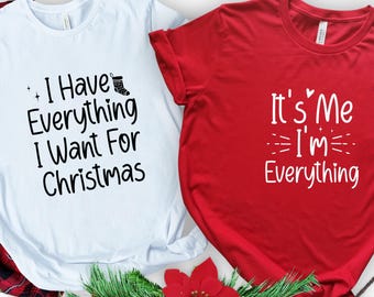 May include: Two t-shirts with Christmas-themed text. One is light blue with the text "I Have Everything I Want For Christmas". The other is red with the text "It's Me I'm Everything". Festive holiday apparel.