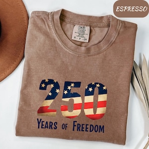 May include: Espresso-coloured t-shirt featuring a distressed American flag design in the shape of the number 250. The text "Years of Freedom" is below the number. The shirt is from Comfort Colors and is size S-P-CH.