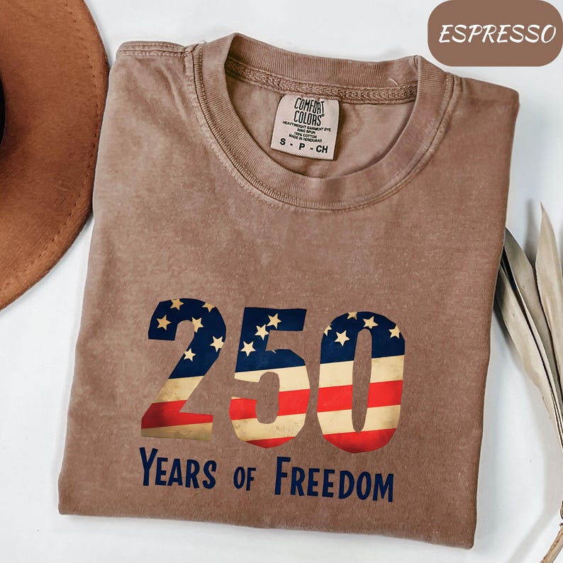 May include: Espresso-coloured t-shirt featuring a distressed American flag design in the shape of the number 250. The text "Years of Freedom" is below the number. The shirt is from Comfort Colors and is size S-P-CH.