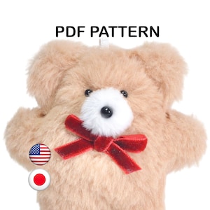 May include: A tan fuzzy teddy bear with a white muzzle, black eyes, and a red velvet bow tie. The text PDF PATTERN is displayed at the top, with small circular icons of the United States and Japanese flags positioned on the left side of the bear.
