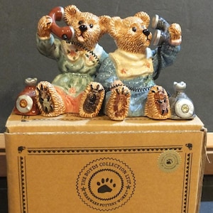 May include: A ceramic figurine featuring two teddy bears seated on a box, each holding a telephone. The bears are dressed in pastel-colored clothing. The box has the text "The Boyds Collection Ltd" and "Bears & Hares you can Trust... estb. 1979".