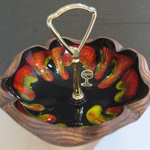 May include: A black and brown ceramic serving dish with a gold metal handle. The dish has a wavy edge and a black glaze with red and yellow swirls. The dish has a "Sequoia Ware" label on the bottom.
