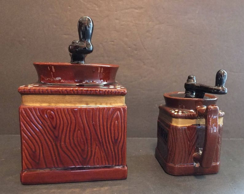 K&ouml;nnte beinhalten: Zwei Kaffeem&uuml;hlen aus Keramik mit Holzmaserung. Die gr&ouml;&szlig;ere M&uuml;hle hat einen schwarzen Griff oben und die kleinere M&uuml;hle einen schwarzen Griff an der Seite.
