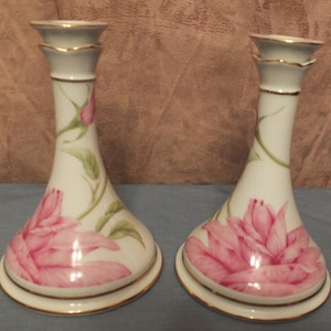 May include: Pair of white porcelain candle holders with pink floral designs and gold accents.