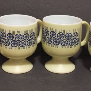 May include: Set of four yellow mugs with blue and white geometric designs. The mugs have a pedestal base.