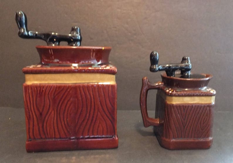 K&ouml;nnte beinhalten: Zwei Keramik-Kaffeem&uuml;hlen mit Holzmaserung. Die gr&ouml;&szlig;ere M&uuml;hle hat eine braune Basis und einen schwarzen Griff. Die kleinere M&uuml;hle hat eine braune Basis und einen schwarzen Griff. Beide M&uuml;hlen haben einen goldenen Rand.
