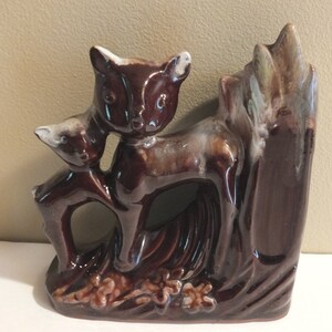 May include: A brown ceramic bookend featuring a mother deer and her fawn standing in a forest setting. The bookend is glazed in a brown and white color scheme.