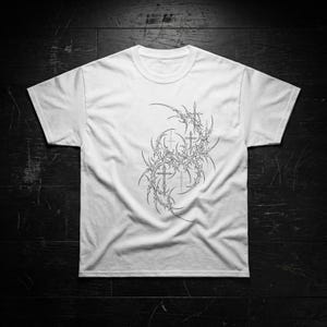 Könnte beinhalten: Weißes T-Shirt mit einem detaillierten schwarz-grauen Grafikdesign auf der Vorderseite. Das Design zeigt eine komplexe Anordnung von stacheligen, organischen Formen und Kreuzen. Das Shirt besteht aus einem weichen Material und hat einen klassischen Rundhalsausschnitt.