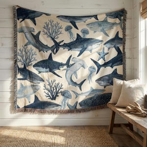 May include: A woven throw blanket with a repeating pattern of sharks, jellyfish, and coral in blue and white. The blanket has a fringed edge. It is displayed on a wall, adding a nautical theme to the room.