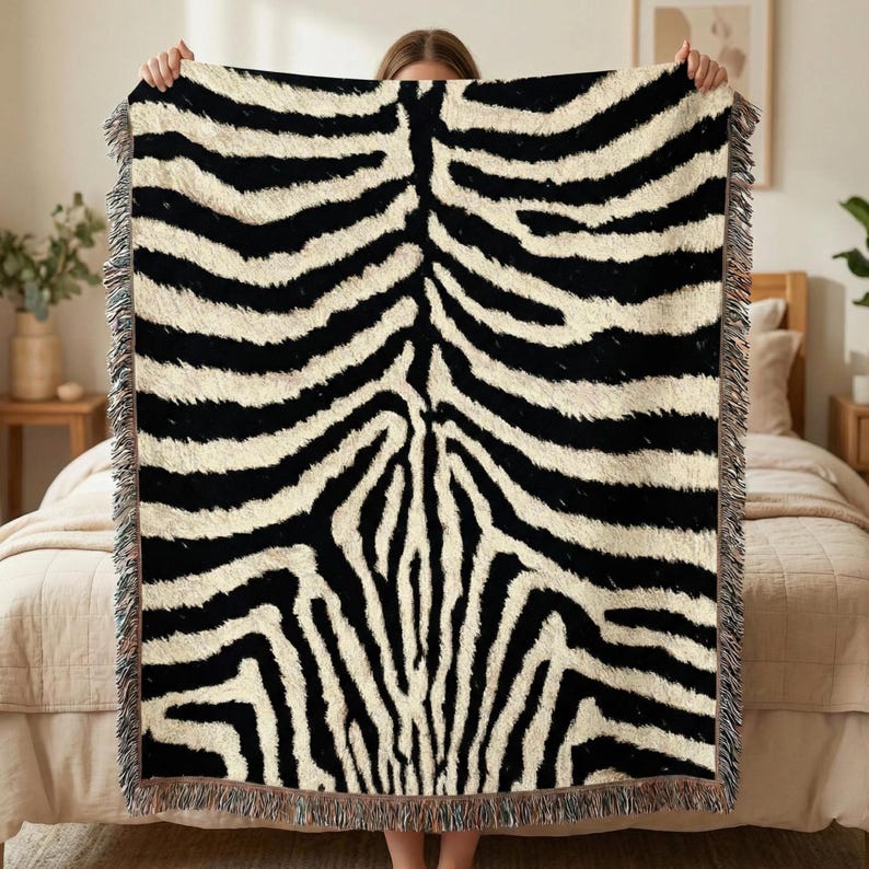 May include: A black and white zebra print throw blanket with fringed edges. The blanket features a bold pattern of black stripes on a cream-colored background, creating a striking visual contrast. This decorative blanket is suitable for a bed or sofa.