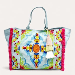 Peut inclure: Sac fourre-tout bleu clair avec broderie florale colorée. Il présente une bordure en franges roses et un pompon multicolore. Le sac a des anses bleu clair et est spacieux.