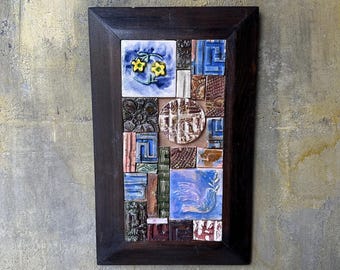 May include: A framed mosaic art piece featuring a variety of colorful ceramic tiles. The tiles depict floral designs, geometric patterns, and a dove with an olive branch. The frame is a dark brown color.