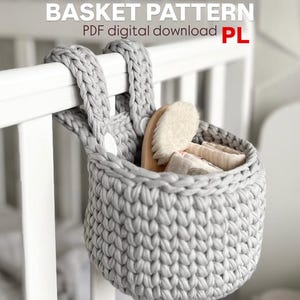 May include: A gray, crocheted basket hanging from a white crib rail. The basket contains a wooden brush and folded items. The text "BASKET PATTERN PDF digital download PL" is at the top of the image.