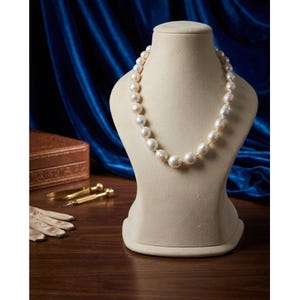 Puede incluir: Un collar de una sola hilera compuesto por numerosas perlas de color blanco roto, forma ovalada y tamaños variados. Las perlas están ensartadas en un bucle continuo, mostrando un brillo natural y una textura superficial lisa en toda la pieza.
