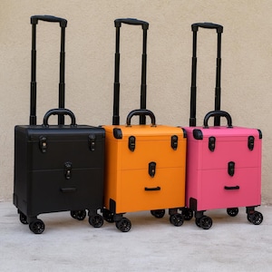 Può includere: Tre valigie con ruote nere, arancioni e rosa. Ognuna ha un manico telescopico nero, una maniglia superiore e quattro ruote. Le valigie hanno una forma squadrata con ferramenta in metallo e un fermo anteriore.