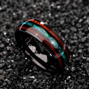 May include: Black ring with a wood grain and opal inlay. The ring has a red and green stripe design. The words "I Love You" are engraved on the side of the ring. This ring is a romantic gift.