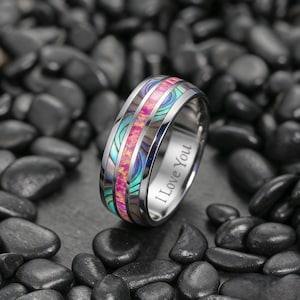 Peut inclure: Une bague en argent avec une incrustation colorée de rose, de turquoise et de matériaux irisés. La bague est gravée des mots "I Love You". La bague est présentée sur un lit de pierres noires.