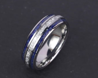 Könnte beinhalten: Ein silberner Ring mit einer blauen Lapislazuli-Einlage und einem gemusterten, strukturierten Silberband. Der Ring hat eine polierte Oberfläche und ein modernes Design. Der blaue Stein hat eine tiefe, satte Farbe.