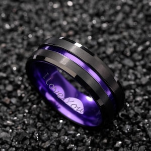 Puede incluir: Un anillo negro con interior morado y una franja plateada. El anillo tiene las palabras "I Love You" grabadas en el interior. El anillo es de metal.