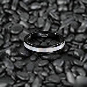 May include: A black tungsten carbide ring with a white mother-of-pearl inlay. The ring has the text "TUNGSTEN CARBIDE" engraved on the inside. The ring is set against a background of dark gray stones.