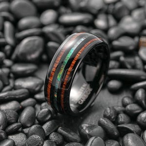May include: A black tungsten carbide ring with a wood inlay and iridescent abalone shell accents. The ring features a polished finish and a comfortable fit. The ring is a stylish accessory for any occasion.