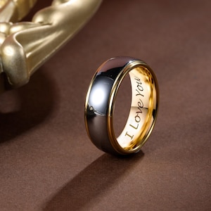 May include: A two-tone ring with a polished silver exterior and a gold interior. The inner band is inscribed with the words "I Love You". The ring has a gold-colored trim.