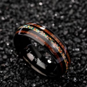 May include: Black ring with a wood grain and opal inlay. The ring has the words "I love you" engraved on the inside. The opal inlay features a variety of colors, including green, orange, and yellow.
