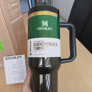 May include: A black and green Stanley Quencher H2.0 tumbler with a handle. The tumbler has a green band with the Stanley logo and the text "THE FLOWSTATE QUENCHER H2.0 TUMBLER 40 OZ". The tumbler is designed for all-day hydration.