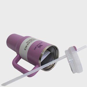 May include: A purple Stanley Quencher H2.0 tumbler with a handle, a white band, and a clear straw. The lid is white with a purple button. The Stanley logo is visible on the side of the tumbler.