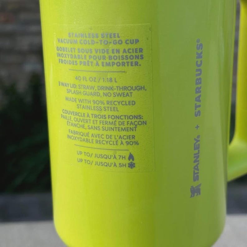 May include: A bright green Stanley + Starbucks vacuum cold-to-go cup. The cup features text including "40 fl oz / 1.18 L" and "3way lid: straw, drink-through, splash guard, no sweat". The cup is made with 90% recycled stainless steel.