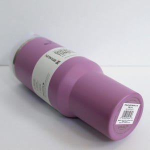 May include: A lavender-colored Stanley Quencher Tumbler with a clear plastic lid. The tumbler has a cylindrical body with a tapered base. A white label wraps around the body with product information. The tumbler is designed for cold beverages.