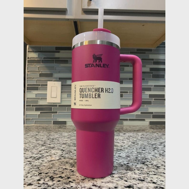 Puede incluir: Un vaso Stanley Quencher H2.0 magenta con tapa y asa blancas. El vaso tiene el logotipo de Stanley y el texto "QUENCHER H2.0 TUMBLER" en el lateral. Est&aacute; dise&ntilde;ado para la hidrataci&oacute;n durante todo el d&iacute;a y tiene una capacidad de 1,18L.