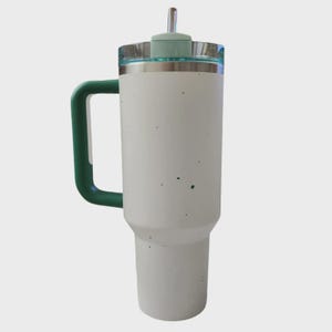 May include: A white insulated tumbler with a green handle and lid. The tumbler has a stainless steel rim and a clear lid with a green top and a straw. The tumbler is designed to keep beverages cold or hot.