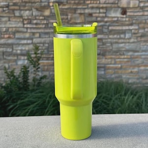May include: A bright neon green insulated tumbler with a handle and a clear lid. The tumbler has a matching green straw and a silver rim. The design is sleek and modern, perfect for keeping drinks cold or hot.