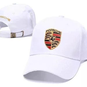 May include: White baseball cap featuring the Porsche logo embroidered on the front. The cap has a curved brim and an adjustable strap at the back. The word "PORSCHE" is embroidered in gold on the back of the cap.
