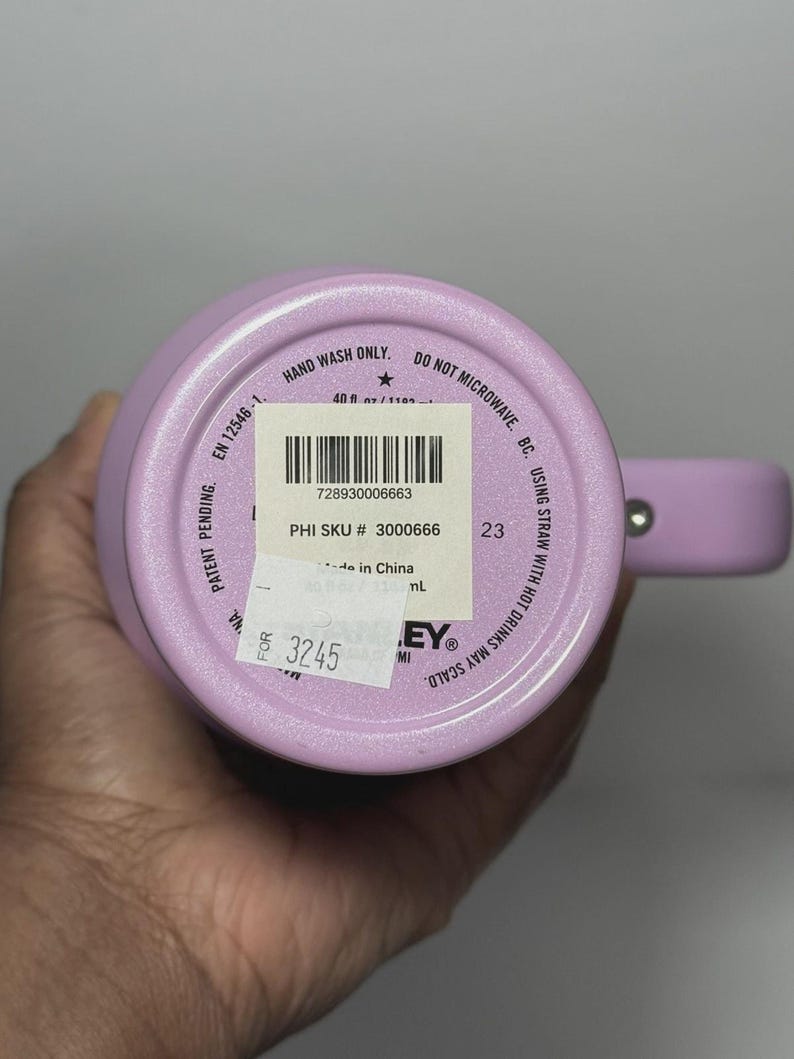May include: A light purple insulated tumbler with a handle. The bottom of the tumbler has a sticker with a barcode and text. The text on the tumbler includes "HAND WASH ONLY" and "DO NOT MICROWAVE".