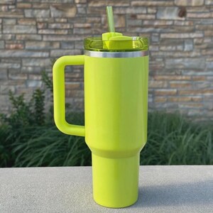 May include: A bright neon green insulated tumbler with a handle, lid, and straw. The tumbler has a silver rim and a clear lid. The handle is a matching neon green color. The straw is also neon green.