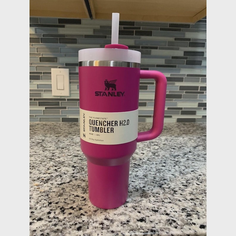 Puede incluir: Un vaso Stanley Quencher H2.0 magenta con tapa y pajita blancas. El vaso tiene un asa y el logotipo de Stanley. El texto "QUENCHER H2.0 TUMBLER" est&aacute; impreso en el lateral. Dise&ntilde;ado para la hidrataci&oacute;n durante todo el d&iacute;a.