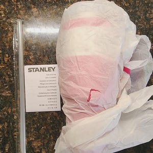 May include: A Stanley product, wrapped in white tissue paper with pink accents. A clear straw and a care instruction card are visible. The card includes the Stanley logo and text in multiple languages.