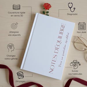 Op de afbeelding: Een wit notitieboek met de tekst "NOTES D'ÉQUILIBRE" in bordeauxrood. Het notitieboek heeft een roosvormige bladwijzer en de tekst "Vers un quotidien équilibré". Er zijn ook illustraties en tekst in het Frans, waaronder "214 pages".